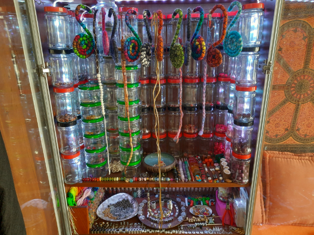 Dreadschmuck in einem Regal: Viele Gläser, Schalen und andere Gefäße mit Dreadperlen in verschiedenen Ausführungen, Materialien und Farben.